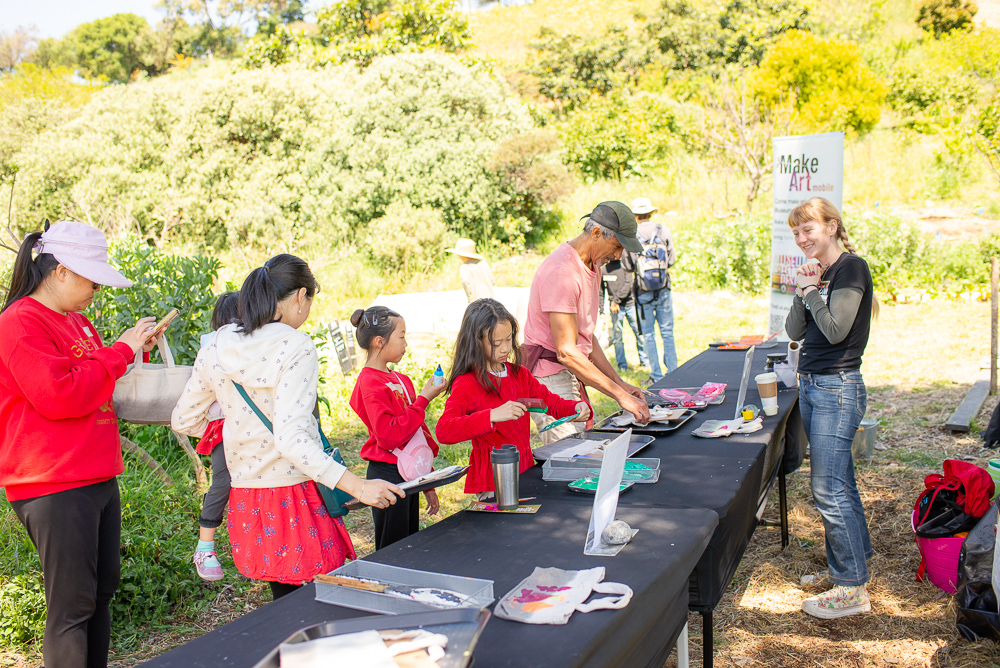 photo of people doing paint prints at a long table in the park