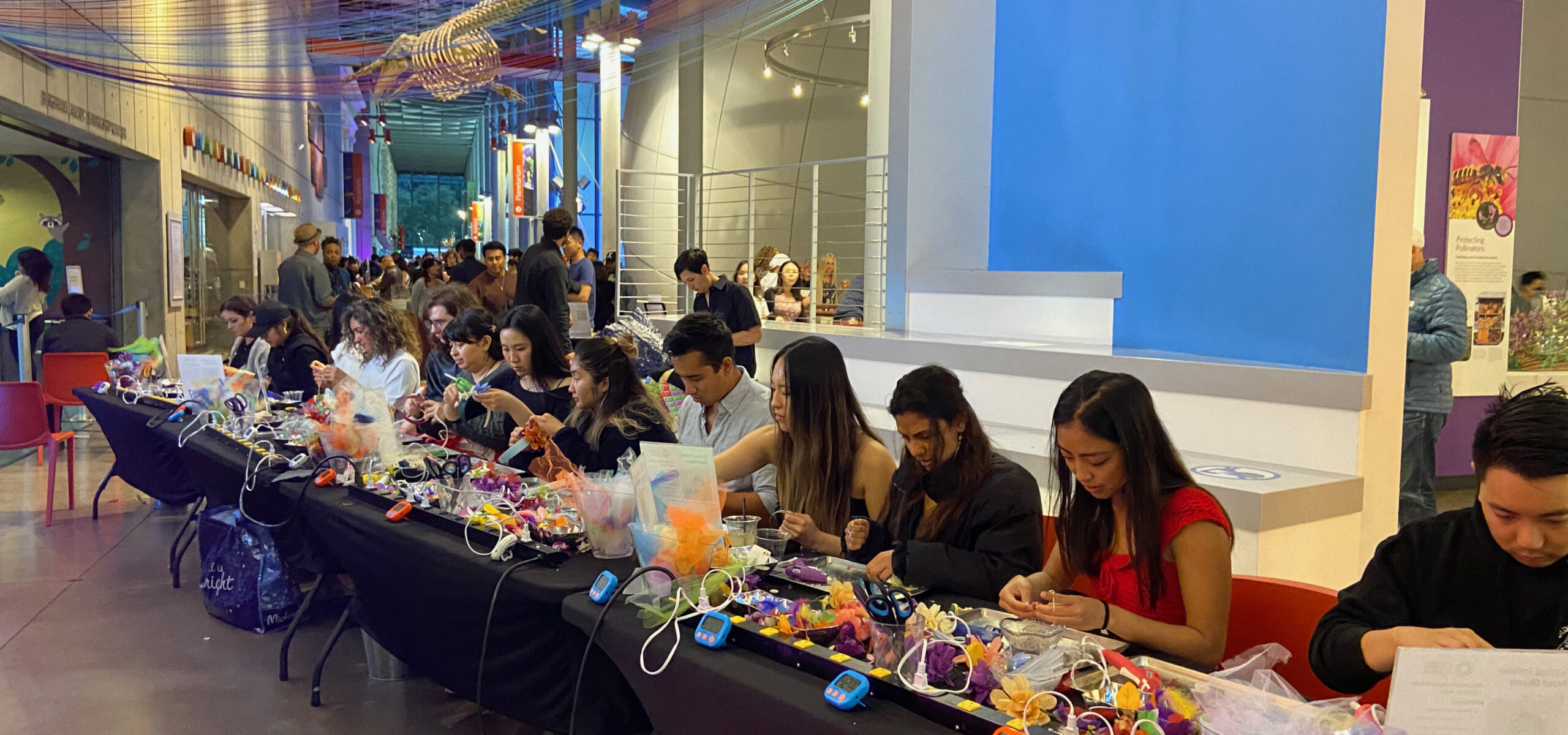 Photo of a long row of people crafting at a table it a big space.