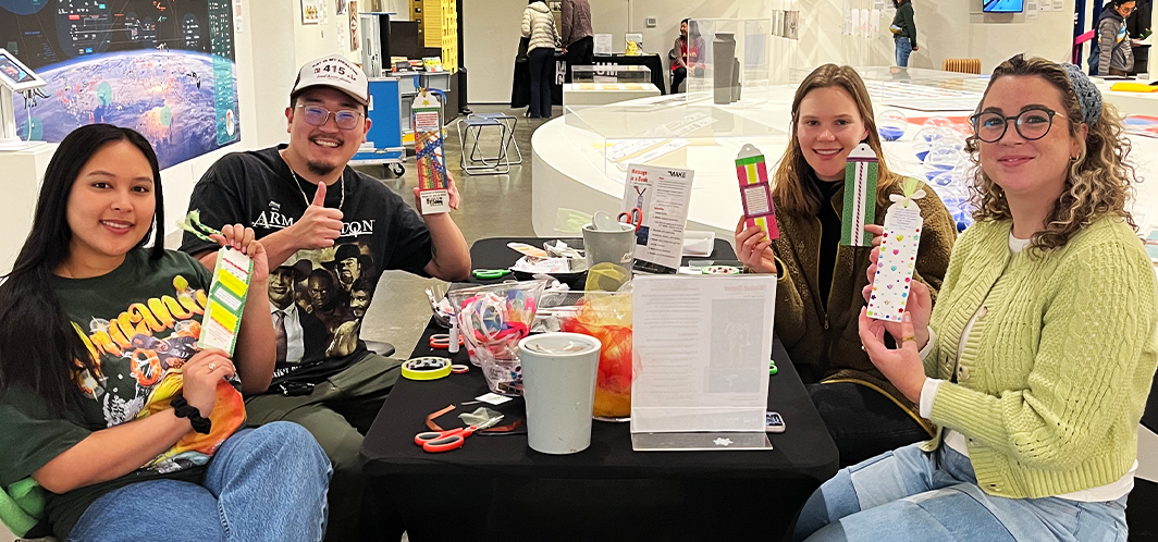 Group of people sitting at a MAKE craft activation table, showcasing their handmade creations.