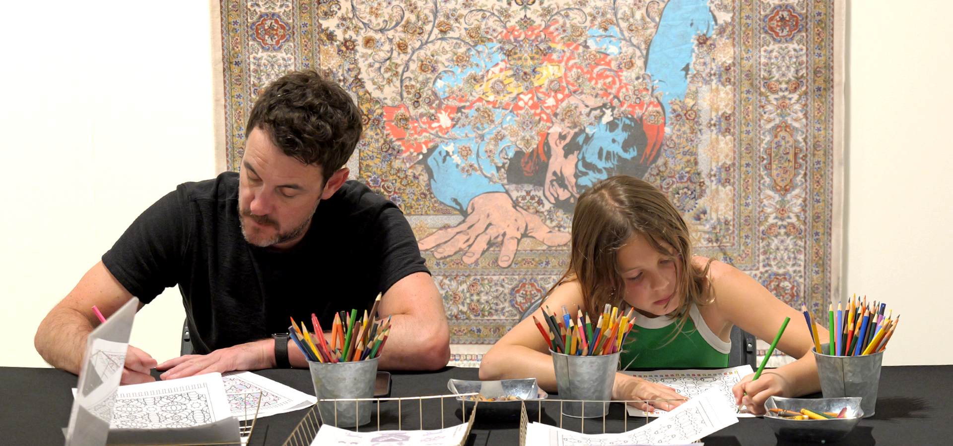 A father and daughter participate in a MakeArt Family Day coloring activity in front of a rug.