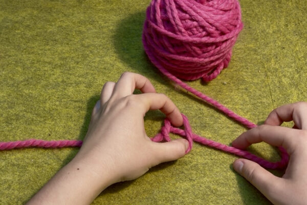 Section 1 - Casting On | Long Tail Method: Step 2 - Tie a Slip Knot: 1. Fold loop over towards the longer end of the yarn. 2. Pinch yarn running underneath your loop.