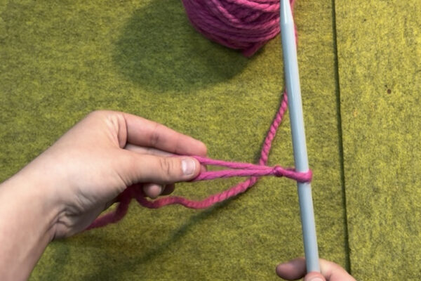 Section 1 - Casting On | Long Tail Method: Step 3 - Cast On: 1. Place slip knot on one of your knitting needles and pull working yarn to tighten. Your loop should be just tight enough to remain on the needle, but loose enough to slide up and down. 2. Adjust slip knot so both working yarn and tail are on the left side of the needle. The tail should be closer to you, and the working yarn further away. 3. Hold needle in right hand. Touch left index finger and thumb together. 4. Place fingers between the tail and working yarn so they form a “V” around your fingers. 5. Spread your fingers to widen the “V” of the yarn strands. Using your remaining three fingers, grab the yarn to create tension in both strands.