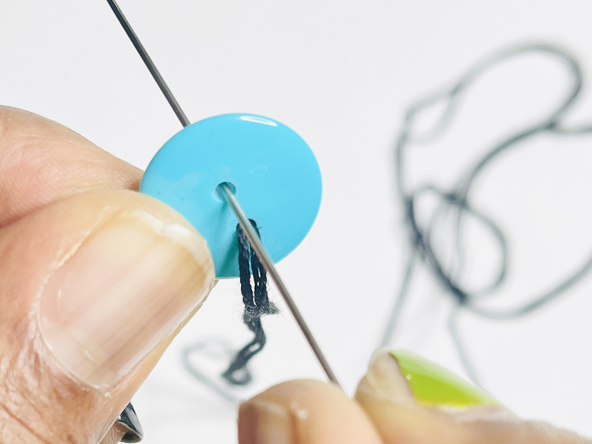 Step 2 - Add the First Button: Place the needle through the second buttonhole and pull.