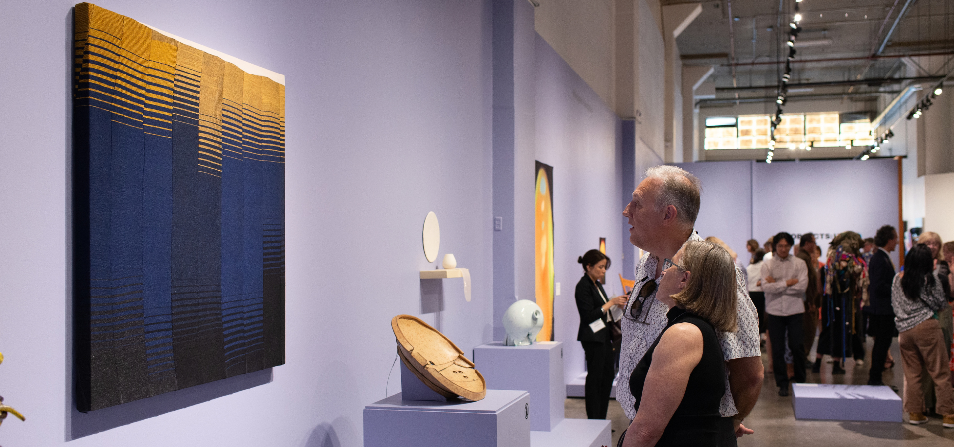 People looking at textile artwork in museum exhibition.